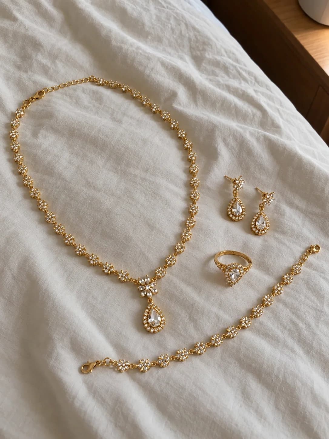 Original product photo of a coordinated gold and diamond necklace, earrings, bracelet, and ring laid on white fabric